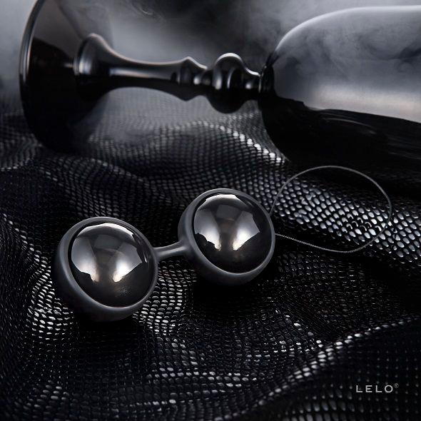 LUNA Beads Noir posées sur un tissu noir texturé, avec un verre en arrière-plan